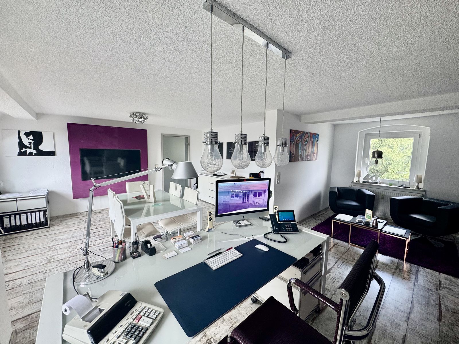 Arbeitsplatz bei DB medien mit iMac, Telefon und Leuchten in Glühlampenform über dem Besprechungstisch